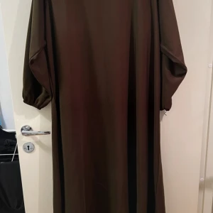 Enkel klänning  - Detta är en enkel brun klänning/abaya den är i storlek S och är lite oversized så den passar även om man har M storlek på bilden har jag tagit med blixt så att man ser hur det ser ut på nära håll. 