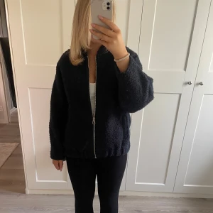 Mörkblå teddyjacka med dragkedja - Mysig mörkblå teddyjacka perfekt för kyliga dagar. Den har en dragkedja framtill och långa ärmar. Jackan är i ett fluffigt material som ger en skön och varm känsla. Perfekt för höst och vinter! Storlek XS-S men sitter som en M
