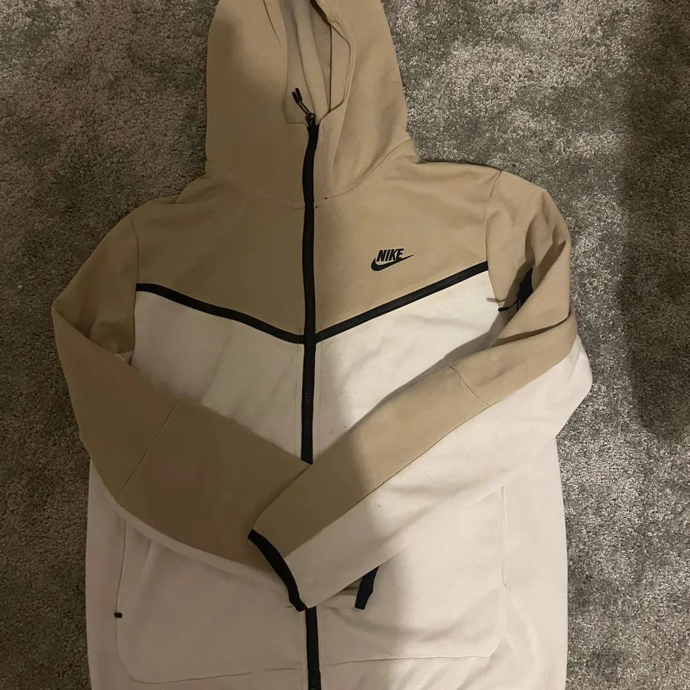 Säljer en snygg och bekväm hoodie från Nike i beige och vitt. Den har en dragkedja framtill och en praktisk huva. Perfekt för höst och vår, med långa ärmar och en stilren design. Passar både till träning och vardag. 🏃‍♂️med byxorna med . Jackor.