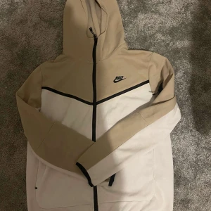 Beige och vit hoodie från Nike - Säljer en snygg och bekväm hoodie från Nike i beige och vitt. Den har en dragkedja framtill och en praktisk huva. Perfekt för höst och vår, med långa ärmar och en stilren design. Passar både till träning och vardag. 🏃‍♂️med byxorna med 