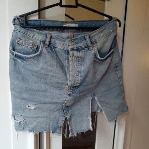 Jeanskjol med slitningar - Säljer en cool jeanskjol med slitningar och råa kanter. Perfekt för en avslappnad och trendig look. Kjolen har en klassisk femficksdesign och en slits framtill. Passar perfekt till sommaren eller en festival!