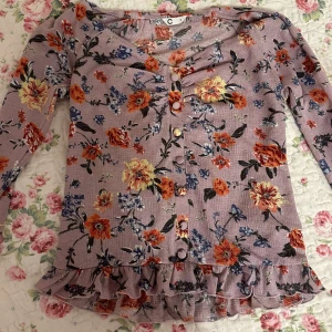 Lila långärmad tröja med blommor - Söt, lila, långärmad tröja med knappar och volanger. 