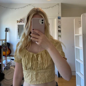 Gul- och vitrutigt croppad topp - Säljer en superfin gul- och vitrutigt croppad topp med korta ärmar. Toppen har en söt knytning framtill och är perfekt för sommardagar. Den är i ett lätt och bekvämt material. Köpt second hand, aldrig använt.