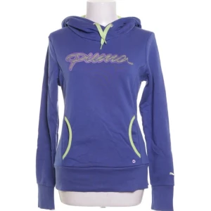 Puma blå lila huvtröja, storlek S - En blå lila huvtröja med en lajm grön insida på huvan. Tröjan har en stor Puma-logotyp på framsidan och en mindre logotyp på vänster ärm och två fickor på framsidan. Det står M i tröjan men den är en S