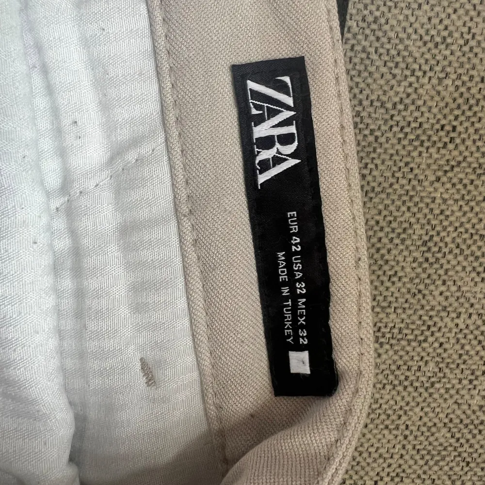 Säljer ett par stilrena beige chinos från Zara. De är i storlek EUR 42/US 32 och tillverkade i Turkiet. Perfekta för både vardag och lite mer uppklädda tillfällen. Byxorna har en klassisk design med fickor fram och bak samt en knapp och dragkedja i gylfen.. Jeans & Byxor.