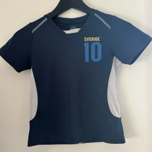 Blå Sverige fotbollströja - Säljer en blå fotbollströja. Tröjan är i barnstorlek, men passar folk med xs. Passformen är som en baby tee.