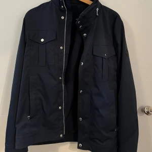 J. LINDEBERG Field jacket - J Lindeberg field jacket. Väldigt stilig med en snygg marinblå färg.  Jackan är i stortsett helt oanvänd och i exemplariskt nyskick! Den är storlek S men passar mig som har M.  Hör av er om ni har några frågor!