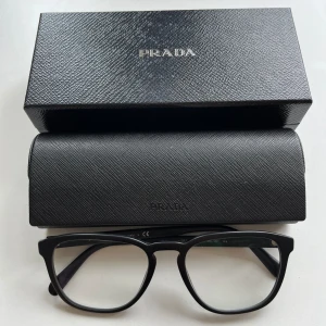 PRADA VPR09V 54 mm glasögon  - Glasögon från PRADA i nyskick. Modell VPR09V, svart matt. Originalförpackning och originaletui medföljer.  Material: acetat, made in Italy  Mått: Linsens bredd: 54 mm Näsbryggans bredd: 19 mm Skalmlängd: 145 mm