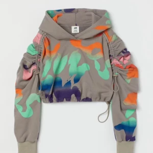 Croppad hoodie - Skick: Nyskick Utseende: Grundfärg grå, neonfärgat graffitimönster, åtdragbara spännen i midja och ärmarna för att skapa olika lookar, slutar över naveln, justerbar längd på ärmar, justerbart midjemått Märke: H&M studio, Limited Edition, sold out