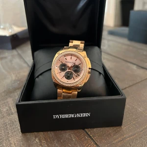 Guldfärgad klocka från Dyrberg/Kern - Säljer en snygg guldfärgad klocka från Dyrberg/Kern. Klockan har en elegant design med en glittrig urtavla och tre mindre urtavlor inuti. Armbandet är i metall och det finns extra länkar med i förpackningen. Perfekt för festliga tillfällen!