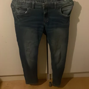 Blå jeansbyxor - Snygga blå jeansbyxor med klassisk femficksdesign och slitna detaljer. Byxorna har en normal passform och är perfekta för en avslappnad stil. De har en dragkedja och knappar framtill.