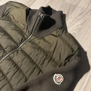 Olivgrön Cardigan från Moncler - Snygg olivgrön dunjacka från Moncler med dragkedja och ribbade detaljer. Jackan har långa ärmar och en quiltad design framtill.  Storlek M men denna modell är mindre i storleken. äkta( köpt från merchsweden) Kan skicka fler bilder i pm. Pris kan diskuteras 