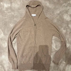 Cashmir hoodie från Davida - Säljer en beige  hoodie från Davida. Den har dragkedja framtill. Tröjan är långärmad och tillverkad i 100% Kashmir som ger en skön känsla. Den är sällan använd och har inga nopror. Hör av er vid funderingar. Nypris ca 3000