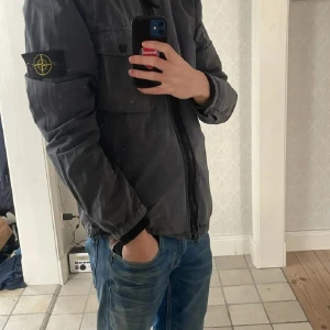  overshirt från Stone Island - Säljer en blå / grå overshirt från Stone Island med dragkedja och en bröstficka. Inte så bra skick många skador och några hål i den så inte något nyskick direkt men inget man tänker på när den är på skulle jag säga