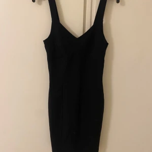 Svart klänning med breda axelband - Snygg svart klänning med breda axelband och en figurnära passform. Perfekt för en stilren look. Klänningen har en enkel design som gör den lätt att matcha med olika accessoarer.