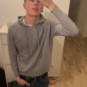 Grå hoodie - Säljer en stilren grå hoodie med dragsko i huvan. Perfekt för en avslappnad look. Tröjan har långa ärmar och är tillverkad i ett mjukt material som ger en bekväm passform.