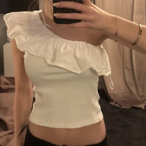 Vit ribbad offshoulder topp - Säljer en söt vit ribbad offshoulder topp med volangdetaljer. Från Zara