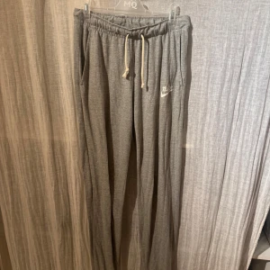Grå mjukisbyxor från Nike - Snygga grå mjukisbyxor från Nike med elastisk midja och snörning. Byxorna har en avslappnad passform och är perfekta för en chill dag. De har fickor på sidorna och en liten Nike-logga på benet.