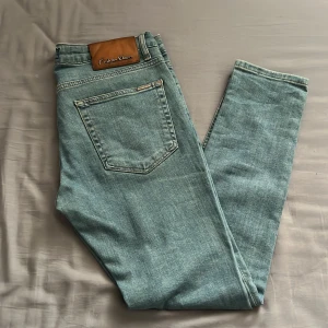 Blå jeans från Calvin Klein - Snygga blå jeans från Calvin Klein med klassisk femficksdesign. Tillverkade i en bomullsblandning med lite stretch för extra komfort. Märkeslogga på bakfickan och en läderpatch med Calvin Klein på linningen. Perfekta för en stilren look.