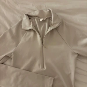 Beige långärmad tröja med dragkedja - Snygg beige långärmad tröja med dragkedja framtill. Perfekt när du ska träna! De har tränings material och sitter tajt och fint 