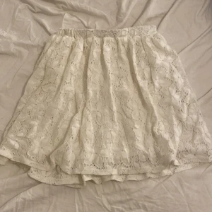 Vit spetskjol - Charmig vit spetskjol med blommigt mönster och elastisk midja. Kjolen har ett innerfoder i satin som ger en mjuk känsla mot huden. Perfekt för sommaren 💕står inte storlek men passar xs-L eftersom midjan är stretch och elastisk⭐️