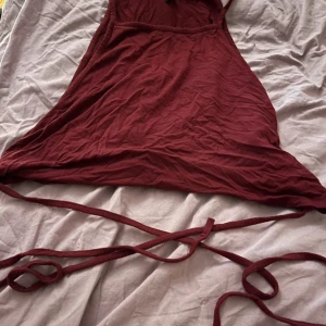 Vinröd topp med knytband - Snygg vinröd topp  med knytband i midjan. Perfekt för en elegant look. Topp har en enkel design med smala axelband och en mjuk, flödande passform.