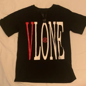 Svart t-shirt från VLONE - Snygg svart t-shirt från VLONE med stort tryck i vitt och rött på framsidan. Tillverkad i 100% bomull och gjord i USA. Perfekt för en casual look.