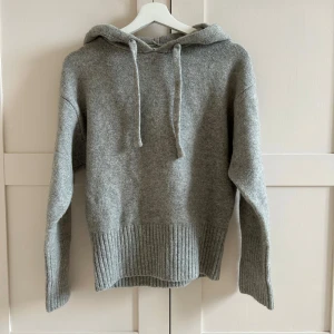  stickad hoodie från Zara - Mysig grå hoodie från Zara i en mjuk och varm ullblandning. Tröjan har en rymlig huva med dragsko och ribbstickade muddar vid nederkanten. Använd ca 2 ggr då den inte passade mig!