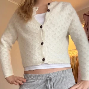 Vit kofta från Zara - Säljer en mysig vit kofta från Zara med ett unikt mönster och knappar framtill. Koftan har långa ärmar och är perfekt för kyligare dagar. Storlek M men jag skulle säga att det är en strök S