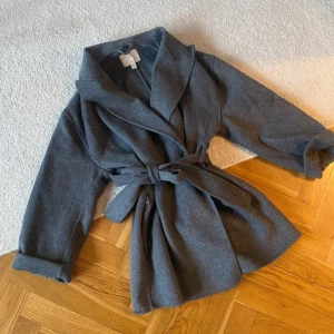 Grå kappa med knytband - Snygg grå kappa i ullmix med knytband i midjan. Knappt använd