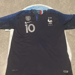 Blå fotbollströja från Nike - Säljer en blå fotbollströja från Nike med nummer 10 och texten 'MBAPPE' på ryggen. Tröjan har korta ärmar och FFF-loggan på bröstet. Perfekt för fotbollsfans!