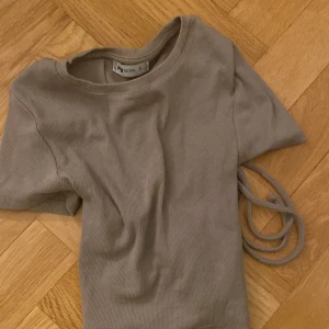 Beige ribbad topp från Sister - Säljer en beige ribbad topp från Sister med korta ärmar och snygg snörning i ryggen. Perfekt för en stilren look. Toppen är i storlek S och har en mjuk och bekväm passform.