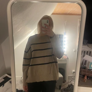 Beige randig tröja från BikBok - Säljer en snygg beige tröja från BikBok med svarta ränder. Tröjan har en avslappnad passform och långa ärmar, perfekt för en stilren look. Den är gjord i ett mjukt material som är jätteskönt 