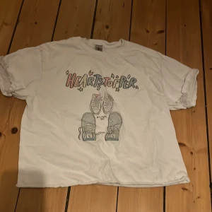 Vit t-shirt med tryck från Gildan - Säljer en vit t-shirt från Gildan med ett färgglatt 'Heartstopper'-tryck och sneakersmotiv på framsidan. T-shirten har korta ärmar och är i en avslappnad passform. Perfekt för en casual look! Köpt från etsy för kanske 1 eller 2 år sen, skulle säga att den passar xs-s💞