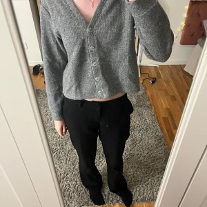 Grå ribbad kofta - Säljer en stilren grå ribbad kofta med v-ringning och knappar framtill. Koftan är croppad och har långa ärmar, perfekt för en avslappnad look.