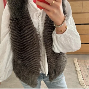 Brun pälsväst - Säljer en snygg brun pälsväst som är perfekt för att lägga till lite stil till din outfit. Västen har ett randigt mönster och är i en normal passning. Den är lätt att matcha med olika toppar och jeans.