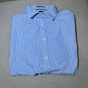 Blå rutig skjorta från Tommy Hilfiger - Snygg blå och vit rutig skjorta från Tommy Hilfiger i slim fit. Skjortan har klassisk krage och knappar framtill. Perfekt för en stilren look. Är nyskick bortsätt från bild 3 (syns inte när man bör plagget) Storlek 32/33 (M/L)