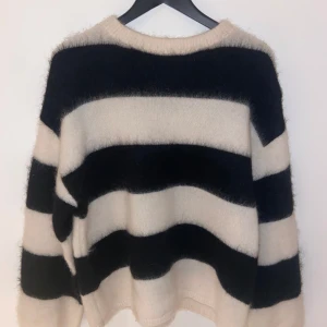 Randig mohair/ull tröja från H&M - Säljer en mysig randig tröja från H&M i en mohair/ull-blandning. Tröjan har breda svarta och beige ränder och långa ärmar. Perfekt för kyliga dagar!
