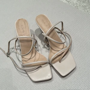Beige sandaler från NA-KD - Stilrena beige sandaler från NA-KD med smala remmar och fyrkantig tå. Sandalerna har en elegant klack och justerbara remmar för perfekt passform. Perfekta för en chic look.