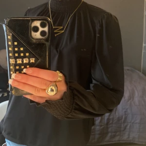 Svart blus från Lindex - Säljer en elegant svart blus från Lindex med smockdetaljer vid hals och ärmslut. Blusen har långa ärmar och en lös passform, perfekt för en stilren look. Passar bra till både jeans och kjol. Inga defekter!