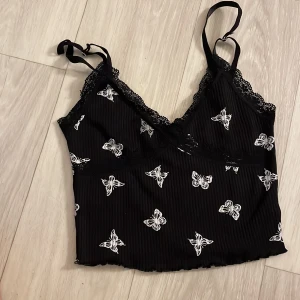 Svart linne med fjärilsmönster, vit ribbad långärmad topp - Säljer ett svart linne från Shein med vita fjärilar och spetsdetaljer. Linnet har justerbara axelband och en omlott-design. Dessutom en vit ribbad långärmad topp med rynkdetalj framtill. Perfekt för olika tillfällen!