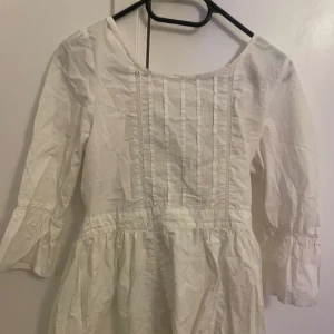 Vit klänning med trekvartsärm - Charmig vit klänning med trekvartsärm och fina veckdetaljer framtill. Perfekt för en somrig look med sin luftiga design.