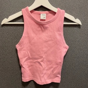 Rosa ribbad tanktop från Bershka - Säljer en söt rosa ribbad linnetopp från Bershka. Toppen är ärmlös och har en tight passform. Den är tillverkad i ett mjukt och bekvämt material. Stl xs. 97% bomull, 3% elastan.