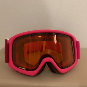 Rosa skidglasögon från Everest - Snygga rosa skidglasögon från Everest med orange tonade linser. Med skydd på insidan för att det ska sitta skönt på ansiktet och ögonen. Perfekta för vinterns äventyr i backen. Justerbart band för optimal passform och komfort. 