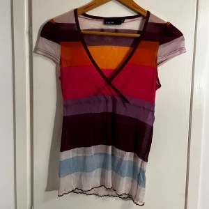 Flerfärgad randig topp från Esprit - Säljer en färgglad topp från Esprit med ränder i olika färger. Toppen har en v-ringad design och korta ärmar, perfekt för en somrig look. Den är tillverkad i ett lätt och bekvämt material (mesh)🪐🪐🪐