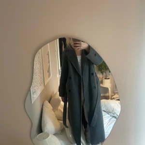 Grå lång kappa - Säljer en stilren grå lång kappa med dubbelknäppning. Perfekt för kyligare dagar med sin klassiska design och långa ärmar. Ett måste för garderoben!