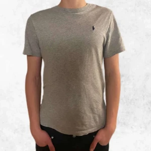 Grå T-shirt från Ralph lauren - Säljer en riktigt snygg grå t shirt från Ralph Lauren. Den är i fint skick utan några synliga defekter. Kragen är lite utsliten. Den är i barnstorlek 14 till 16 vilket är ungefär som en S. Personen på bilden är ca 180 cm. Vid frågor eller funderingar är det bara att höra av sig.