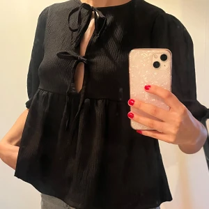 Svart blus  - Snygg svart blus med knytband framtill och trekvartsärmar. Blusen har en lös passform och har aldrig använts och är köpt nyligen. Pris går att diskutera ✨