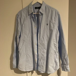 Ljusblå skjorta från Ralph Lauren - Snygg ljusblå skjorta från Ralph Lauren som är i nyskick använd 1 gång. Väldigt skrynklig på bilderna så skulle behöva strykas. Storlek M och passar aningen större