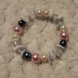 Färgglatt pärlarmband - Charmigt armband med pärlor i olika färger som rosa, blå och vit. Armbandet har även genomskinliga och ljusblå detaljer som ger det en lekfull touch. Perfekt för att liva upp vilken outfit som helst!